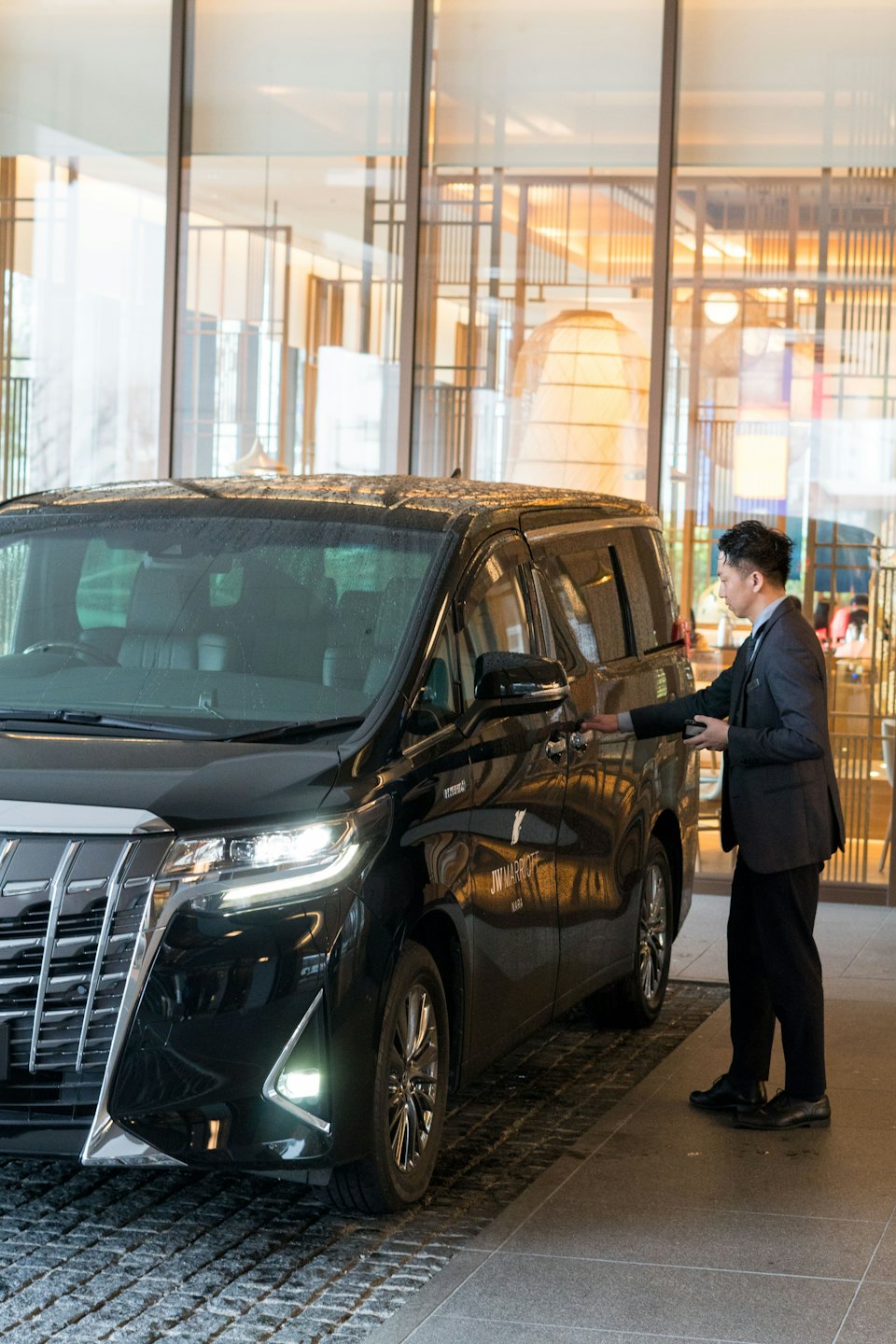 Mann im Anzug öffnet die Tür eines Luxus-Minivans vor einem modernen Gebäude.